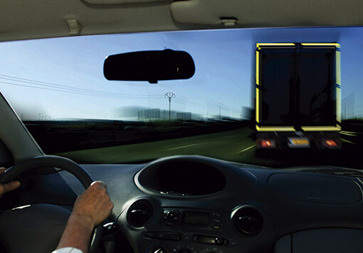 Diagrama que muestra la señalización obligatoria para vehículos largos y pesados en España, incluyendo señalización trasera y lateral con líneas rojas y amarillas. Se detallan ejemplos de camiones y autobuses con áreas específicas marcadas en rojo para la parte trasera y amarillo/blanco para los laterales.